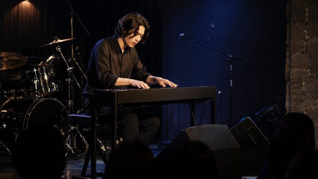 ライブステージでスリムな電子ピアノを演奏する日本人ミュージシャン