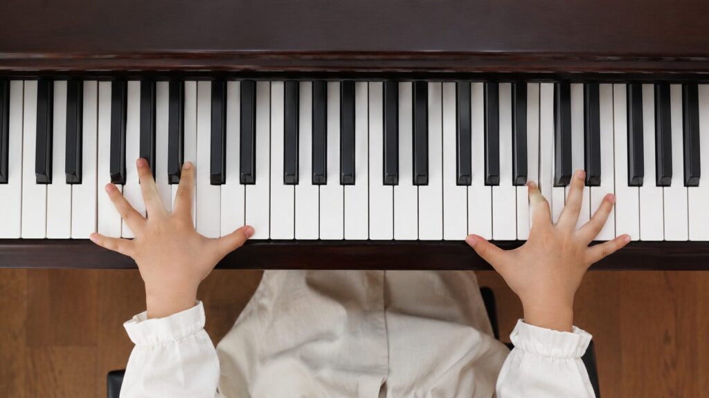 ピアノの鍵盤上で小さな手を広げて届く音程を確認している様子