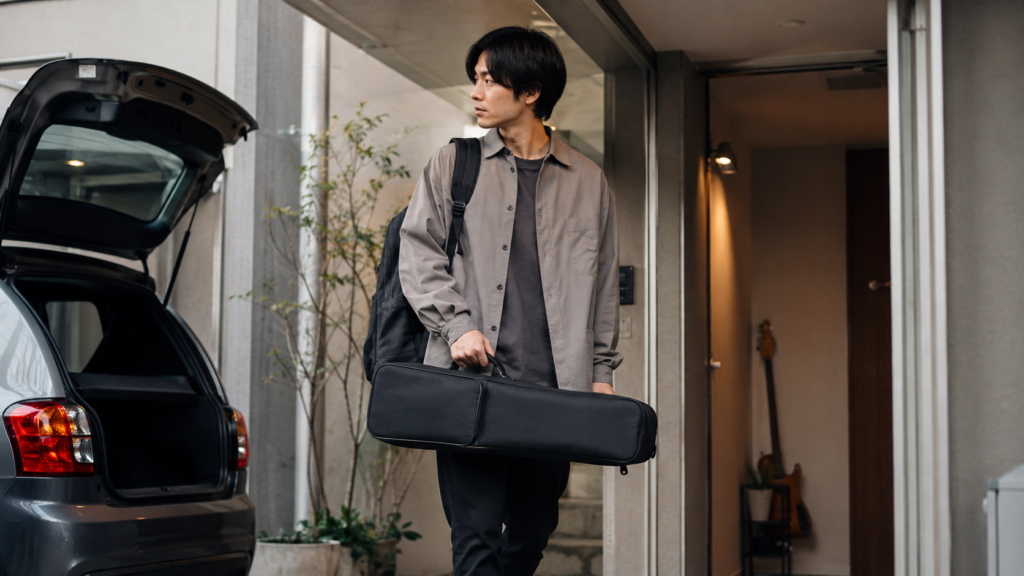 コンパクトなヘッドレスギターケースを持ち運ぶ日本人ギタリスト