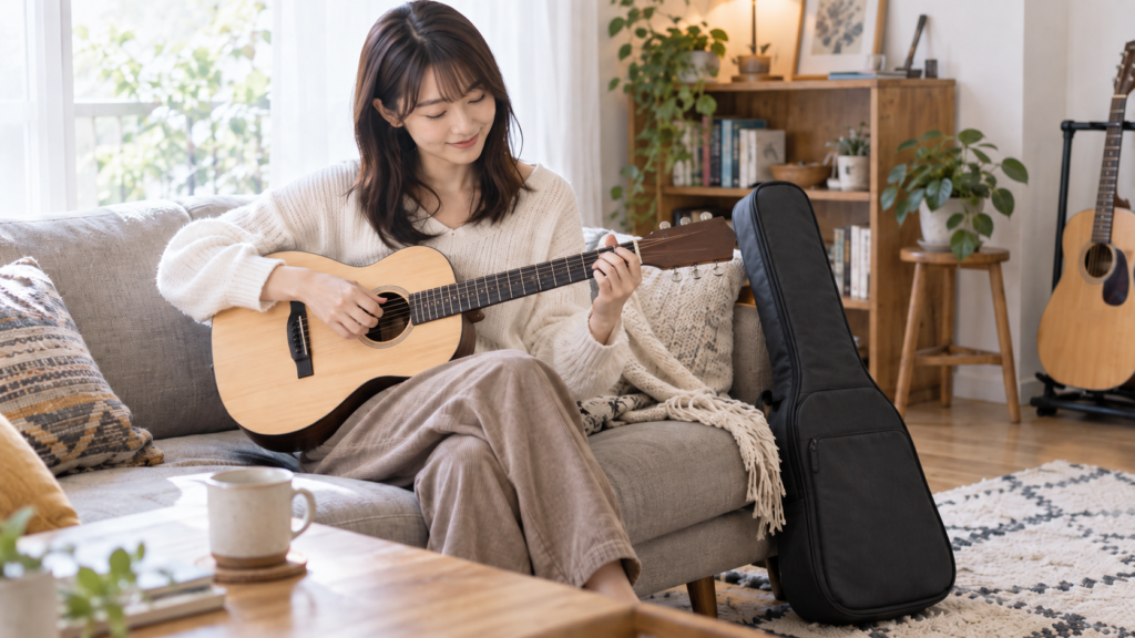 自宅のソファで小ぶりなアコースティックギターを弾く日本人女性